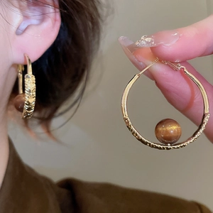 Detailed view of large golden hammered hoop earrings with a brown cat-eye gemstone bead