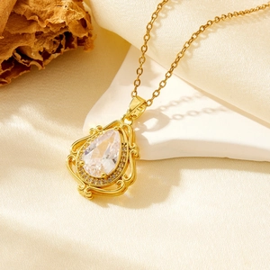Golden water drop pendant necklace with clear crystal on white stone and silk background