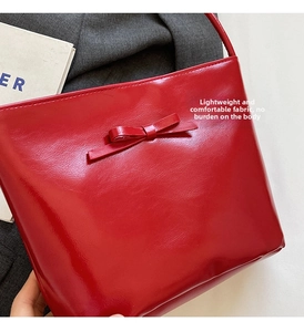 Detail of red glossy leather shoulder bag featuring a decorative matching bow accent