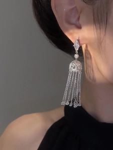 Close-up of diamond-studded geometric tassel earrings worn by a model in natural light