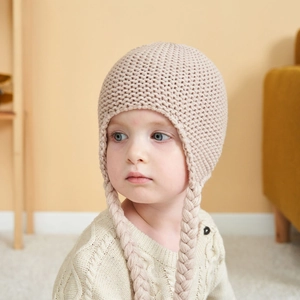 Close-up detail of knitted baby hat with soft beige wool texture and braided ear flaps