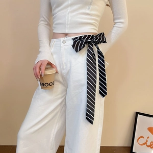 Close-up of a black and white striped satin scarf tied as a bow belt on white trousers