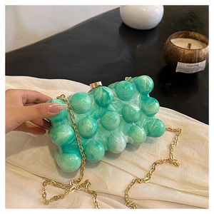 Détail d'un sac de soirée sphérique en acrylique vert marbré avec une élégante chaîne dorée