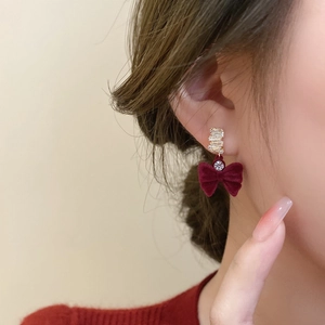 Boucles d'oreilles nœud en velours rouge dorées avec zircons portées par un modèle
