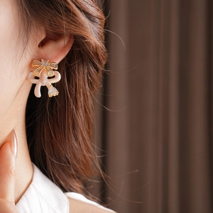 Detail view of gold bow earrings with white enamel and sparkling zircon on a model
