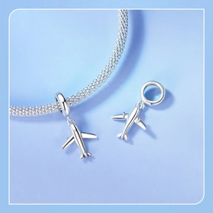 Close-up of a silver airplane charm attached to a metallic mesh braided bracelet