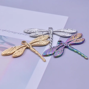 Three dragonfly pendants in gold, silver, and rainbow steel finishes on light purple background