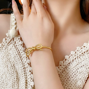 Dettaglio del bracciale rigido dorato con fiocco al polso con una luce soffusa