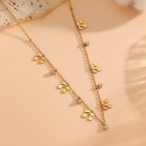Detail of 18K gold-plated necklace with hollow hearts and crystals on warm beige background