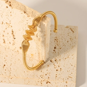 Detailed shot of 18K gold plated wire-wrapped knot bangle on a travertine stone