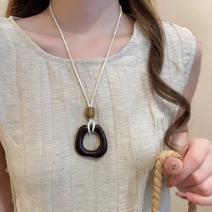Detail of wax rope necklace with brown resin pendant and amber bead on linen vest