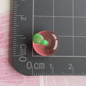 Macro shot of 1.5cm pink translucent resin apple charm on scale ruler background