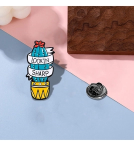 Macro detail of cartoon cactus enamel pin with 'Lookin Sharp' text and metal butterfly clutch