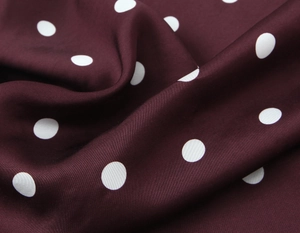 Macro shot of dark burgundy satin fabric with white polka dots showing smooth texture