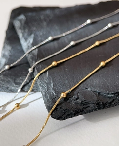 Close-up of gold and silver snake bone chain necklaces with beads on black stone