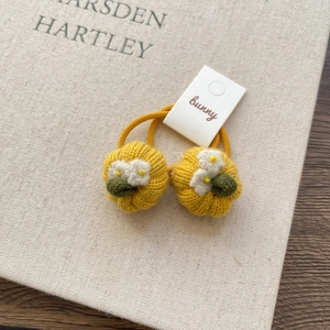 Detail view of two handcrafted knitted pumpkin hair ties on a warm textured background