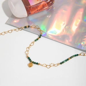 Close-up of gold heart necklace with green stone beads on minimalist white background