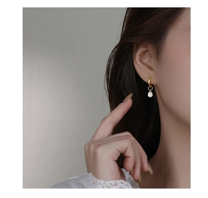 Detail of a minimalist gold hoop earring featuring a clear teardrop zircon pendant on a model