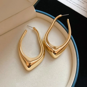Detail of chunky gold U-shaped sculptural earrings in a blue jewelry display box