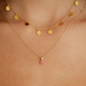 Detail of layered gold S925 silver necklaces featuring pink gemstone and metal discs
