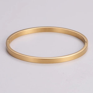 Detailed close-up of a minimalist round bangle with a polished gold finish on grey surface