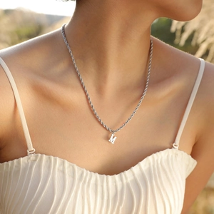 Detail view of a silver letter M pendant on a twisted rope chain worn by a model