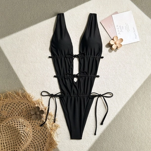 Flat lay of black one-piece swimsuit with cutout details and beach props on textured carpet