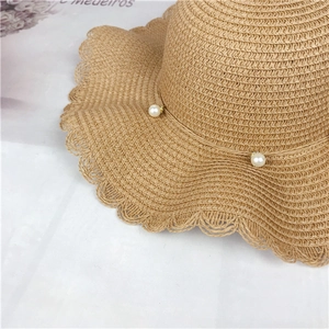 Detail of wide brim straw hat featuring wavy edges and elegant white pearl accents