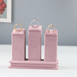 Pink velvet jewelry display stand featuring three gold and silver rings on white desk