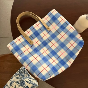 Detail of blue plaid tote bag with brown leather handles and sturdy metal rivets