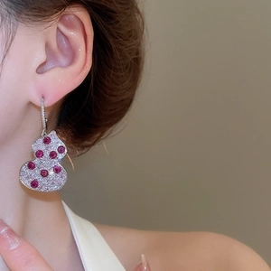 Macro side view of C-shaped gourd earrings with red stones and cubic zirconia on model