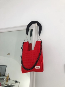 Detail of red hollow crochet handbag featuring thick black chain and brand label