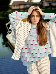 Détail d'un pull en tricot bleu clair avec motif de voilier rouge et blanc et poignets côtelés