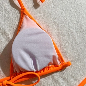 Detailed interior of orange bikini top featuring removable pad slots and edge stitching