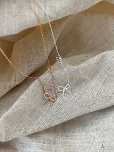 Detailed close-up of double bow pendants in gold and silver finish on soft beige fabric