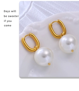 Macro view of gold U-shaped hoop earrings with large lustrous white hanging pearls
