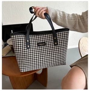 Detail of houndstooth tote bag showing fabric texture, leather trim and gold rivet accents