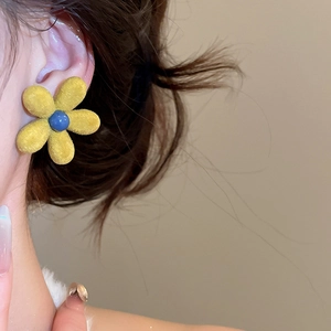 Close-up of yellow flocked flower earring with blue center worn by a model
