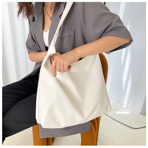 Minimalist white PU tote bag with knotted shoulder strap detail worn by a model