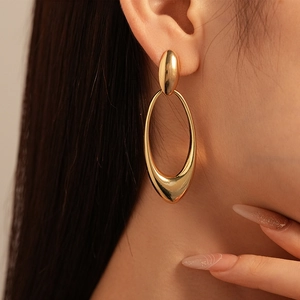 Close-up of golden geometric oval earrings worn by a model showing luxury metallic luster