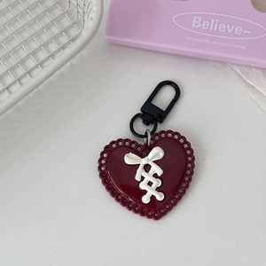 Deep red heart keychain with white ribbon bow and black metal clip on a white table