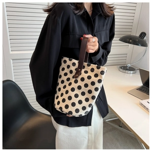 Chic beige polka dot canvas bucket bag with brown leather handle shown in a lifestyle setting