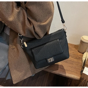 Detail of a black pleated crossbody bag with a gold square twist lock worn by a model