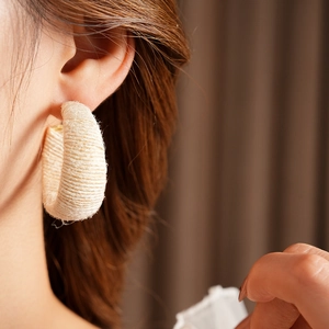 Close-up of beige woven yarn texture on large C-shape hoop earrings worn by a model
