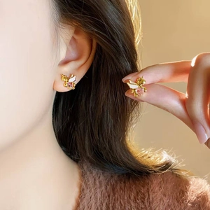 Golden unicorn stud earrings with pink heart gemstone and white enamel wing details