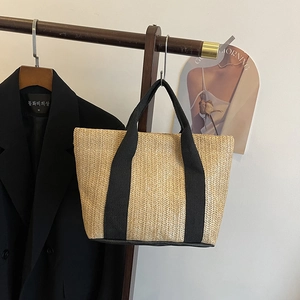 Detail of woven straw tote bag featuring wide black canvas handles on a wooden hanger