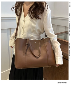 Brown soft leather tote bag with shoulder strap shown on model in a minimalist setting