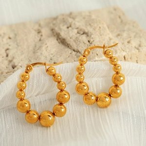 Elegant gold spherical bead hoop earrings on white fabric and natural stone background