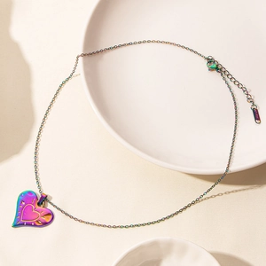 Rainbow heart pendant necklace made of stainless steel resting on a ceramic tray