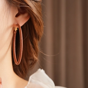 Close-up of woman wearing large brown leather texture hoop earrings with gold clasp